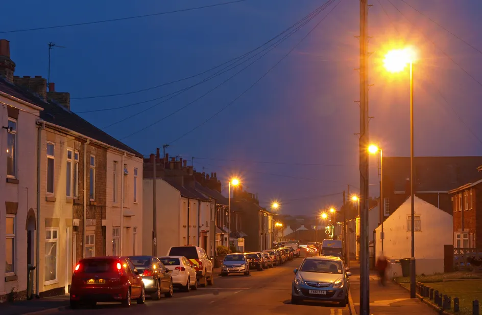 A terraced residential street at dusk under warm street lamps